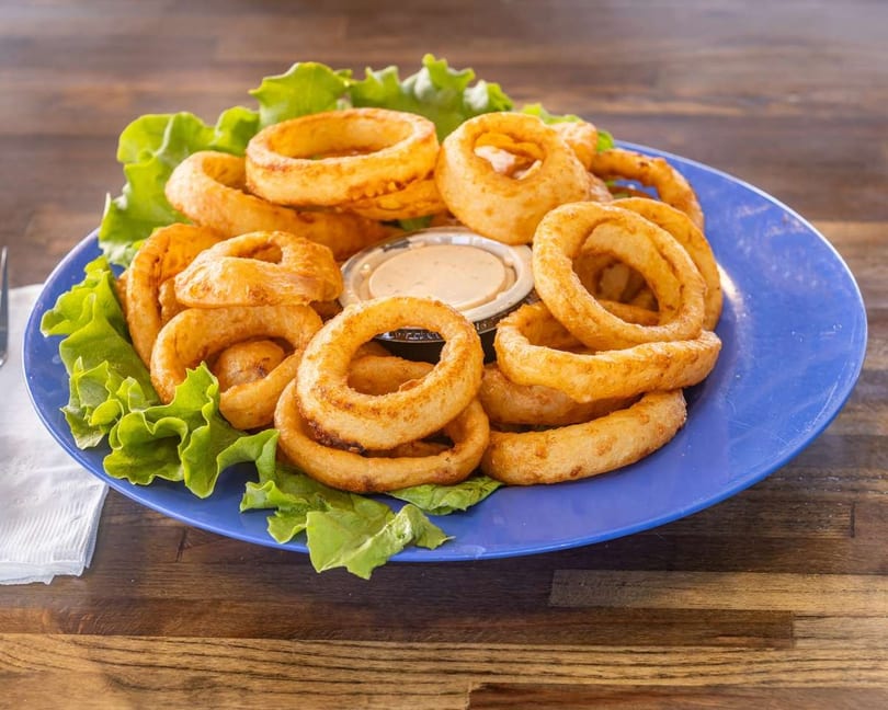 Golden-brown onion rings with two dipping sauces and lettuce on a blue plate.