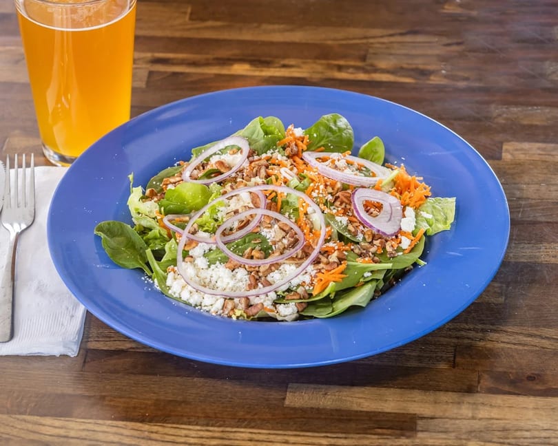 Spinach salad with red onions, shredded carrots, feta cheese, and pecans on a blue plate.