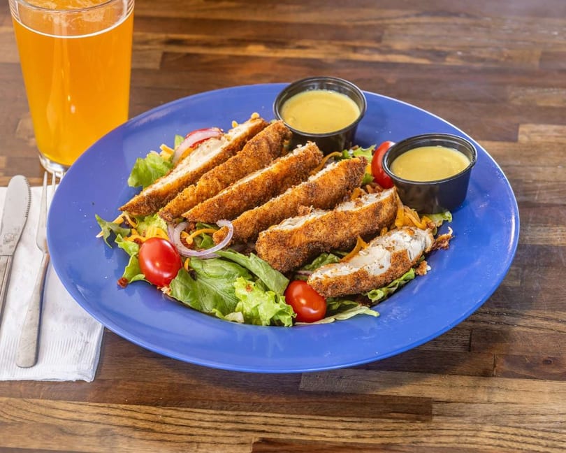 Crispy chicken tender salad with cherry tomatoes, red onion, and two cups of dressing.