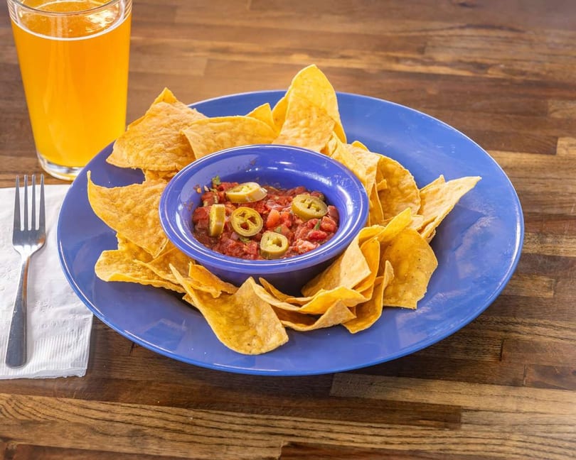 Crispy tortilla chips and salsa with jalapeños on a blue plate, next to a glass of beer.