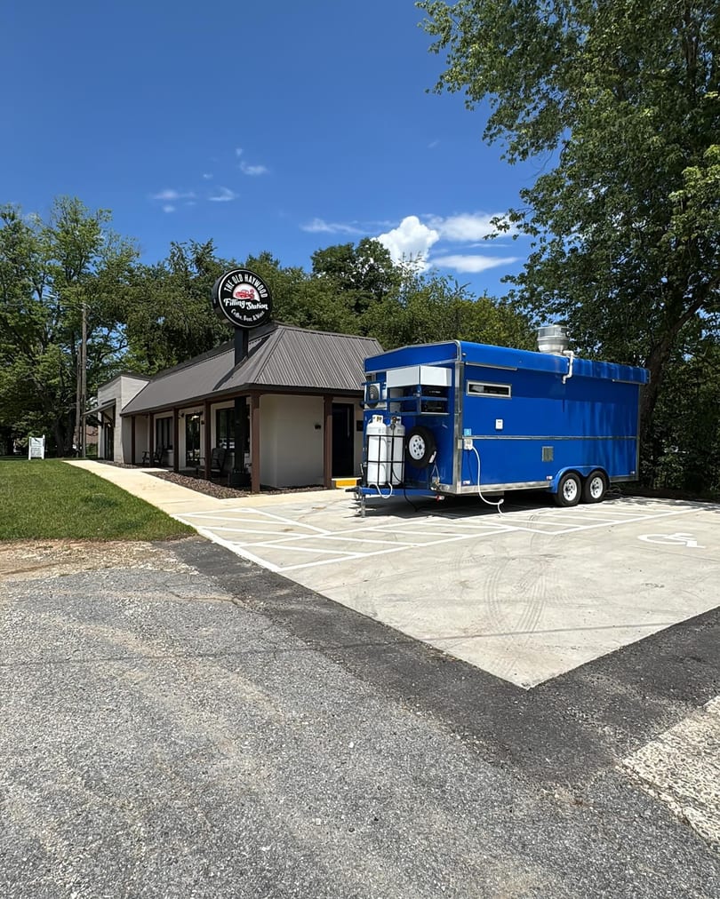The Old Haywood Filling Station building with a blue food truck parked in front.